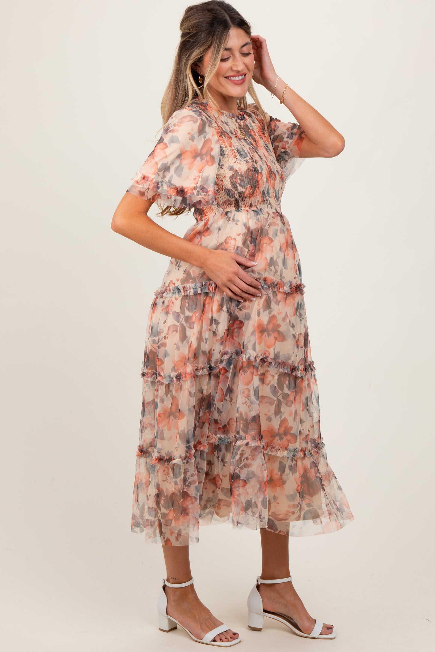 woman wearing a floral chiffon maternity dress with tiered layers and a baby bump, standing and holding her belly