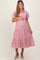 woman wearing a pink embroidered maternity dress with a square neckline and tiered skirt, holding her baby bump