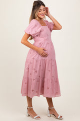 woman wearing a pink maternity dress with puff sleeves and eyelet details, gently cradling her baby bump