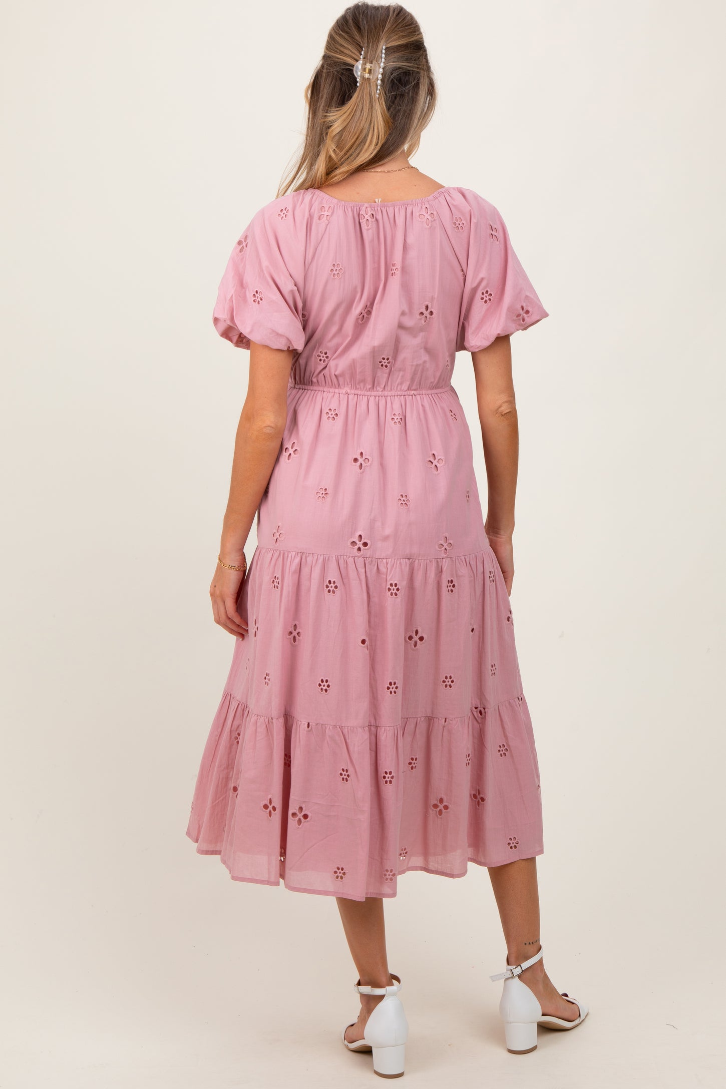 woman wearing a pink maternity dress with short puff sleeves and floral embroidery, showing a gathered waist and tiered skirt