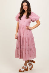 woman wearing a pink tiered maxi dress with puff sleeves and floral embroidery, standing and smiling