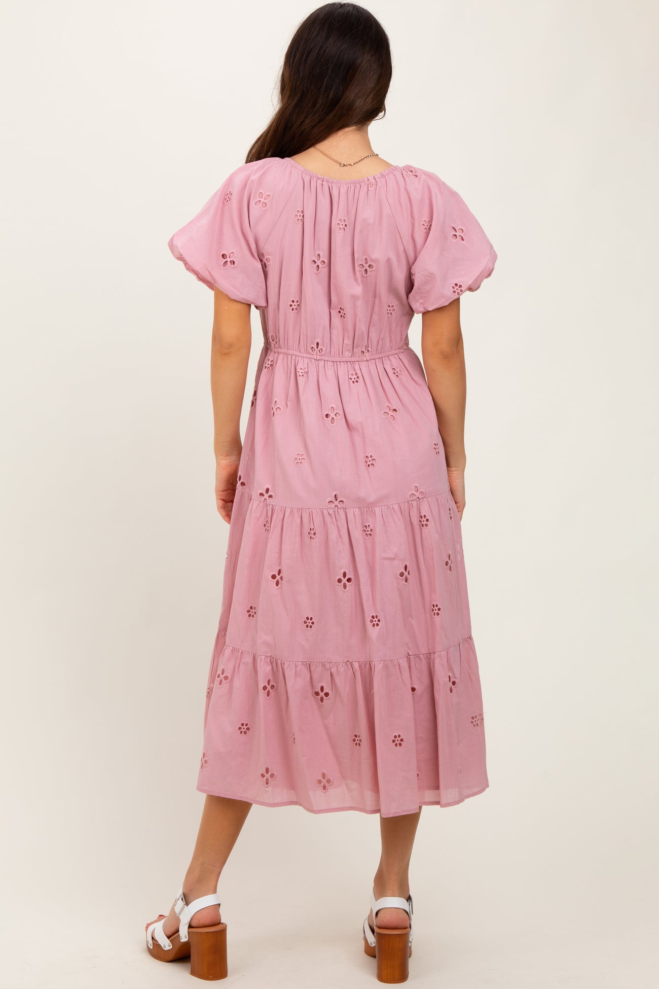 woman wearing a pink tiered maxi dress with floral embroidery and puff sleeves, showing the back detail