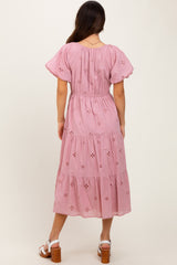 woman wearing a pink tiered maxi dress with floral embroidery and puff sleeves, showing the back detail