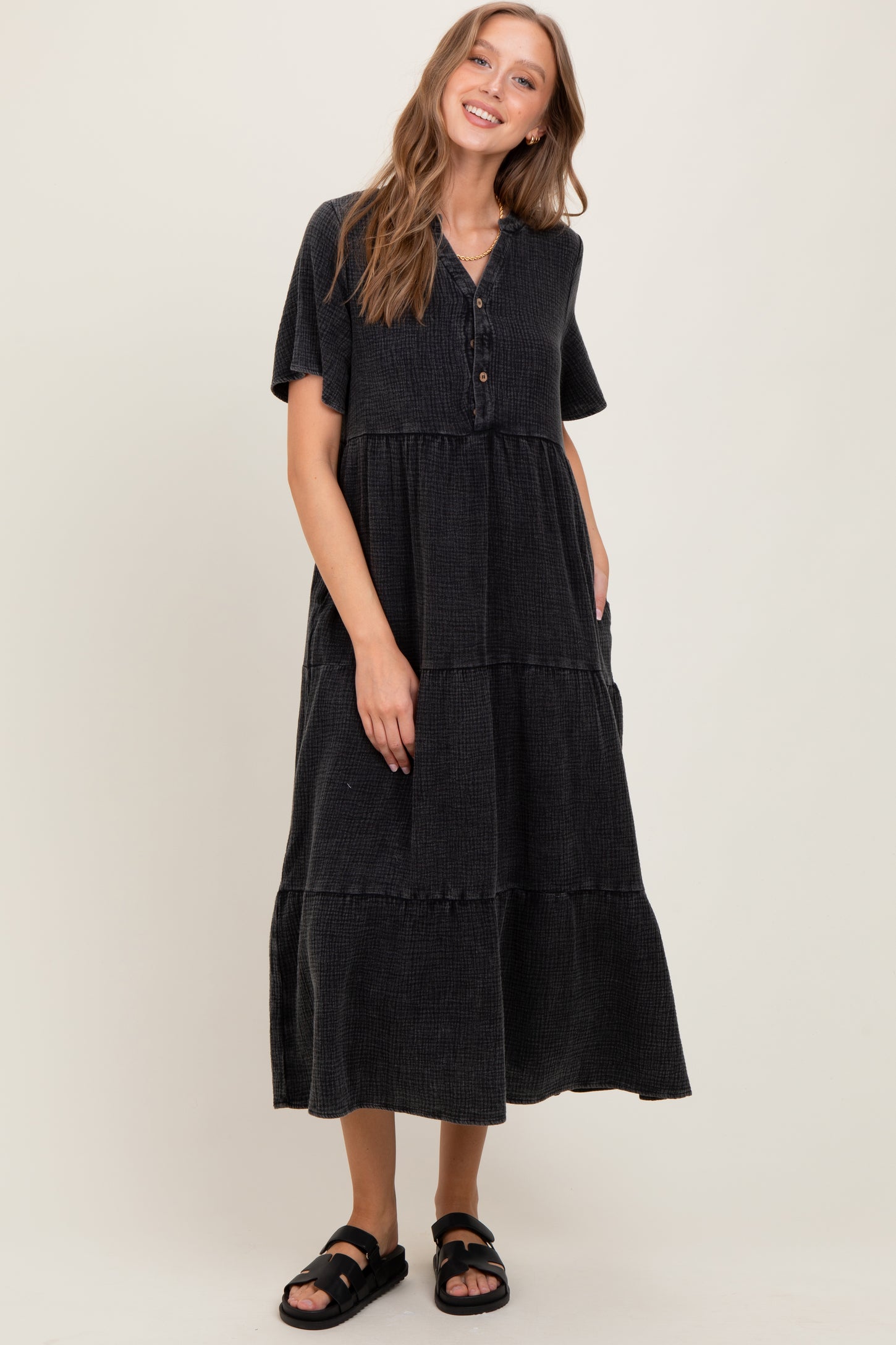 woman wearing a black tiered maxi dress with short sleeves and buttons, standing and smiling