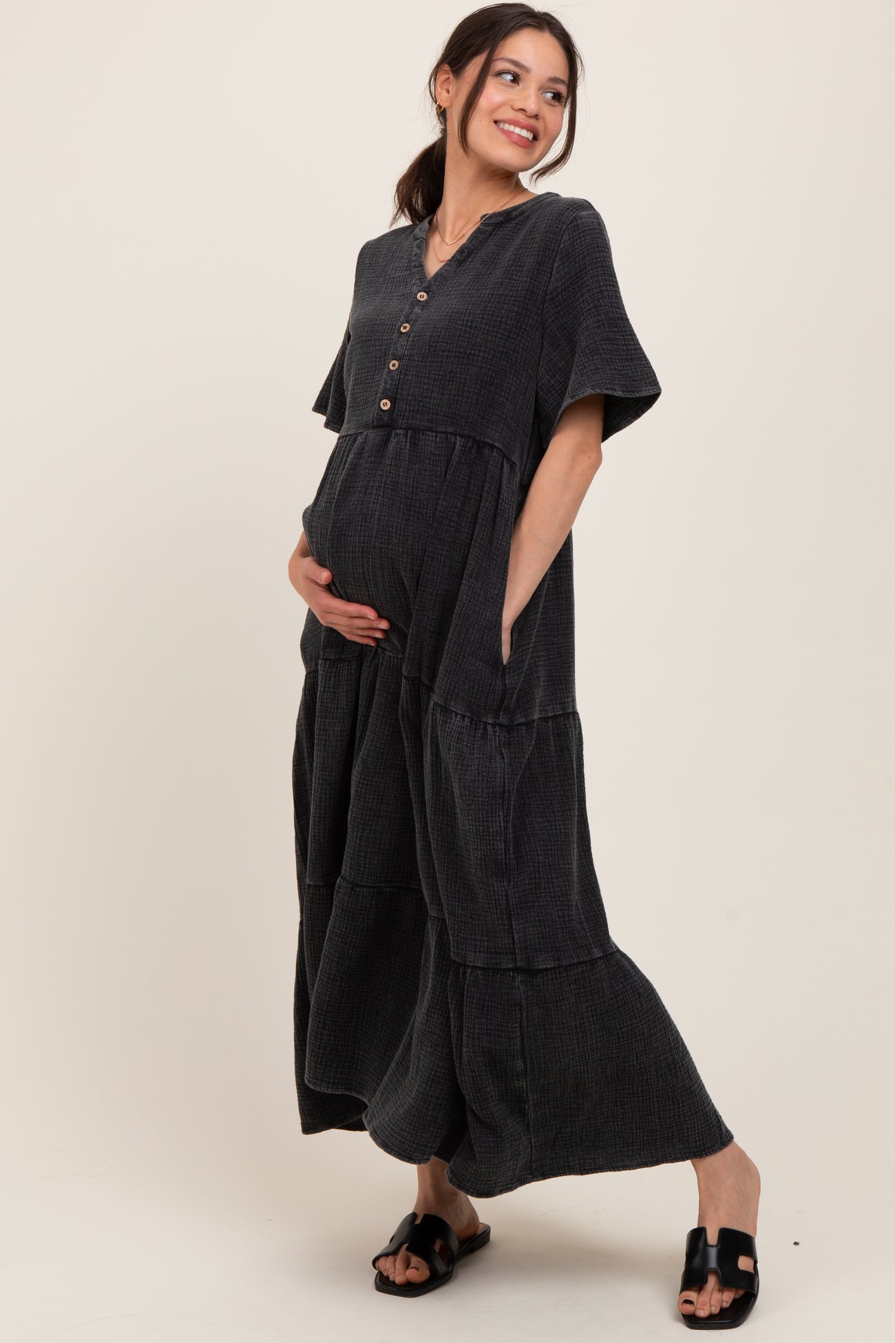 woman wearing a dark gray short sleeve maternity dress with buttons and pockets, cradling her baby bump
