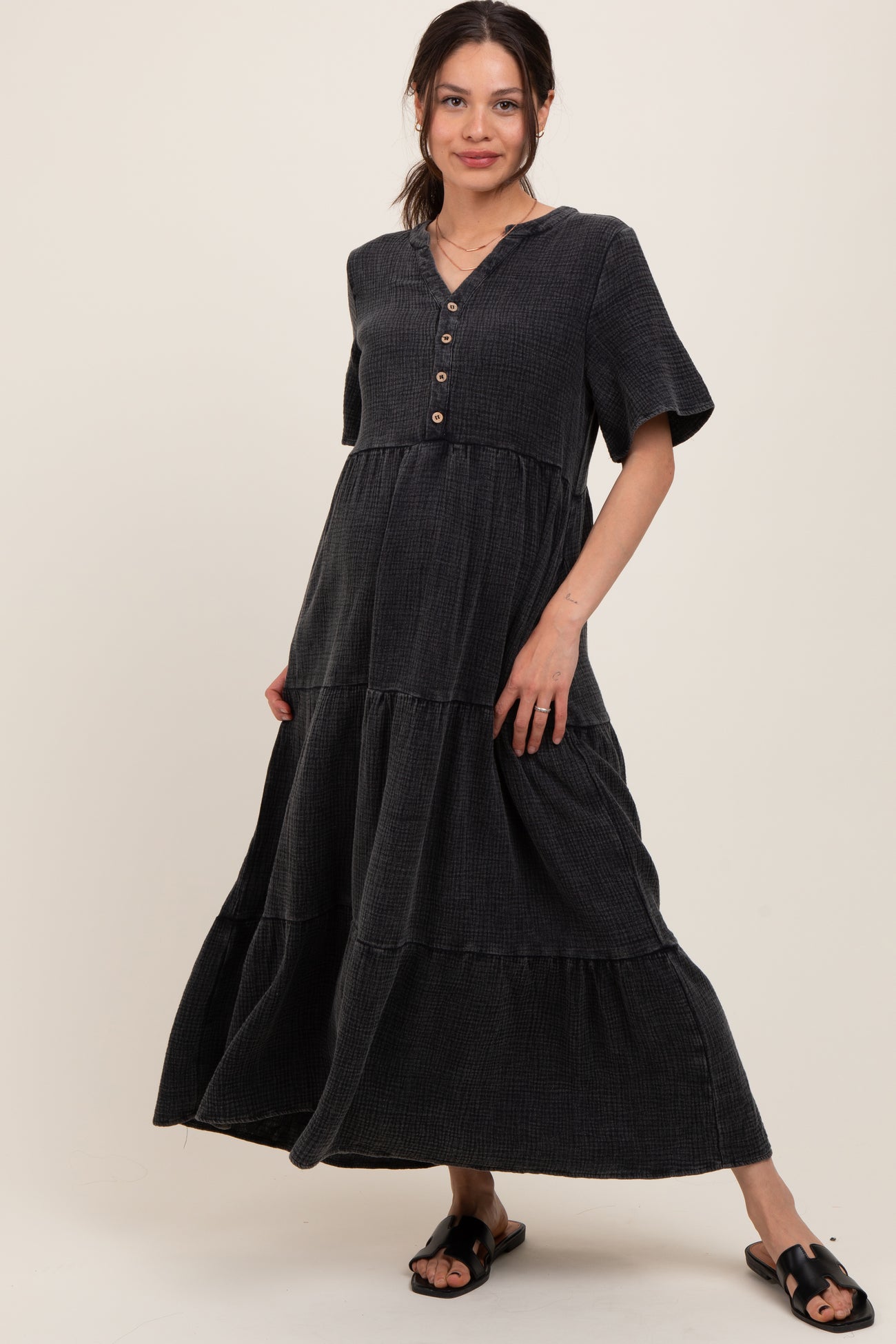 woman wearing a black tiered maternity dress with short sleeves and button details, standing in a relaxed pose