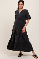 woman wearing a black tiered maternity dress with short sleeves and button details, standing in a relaxed pose