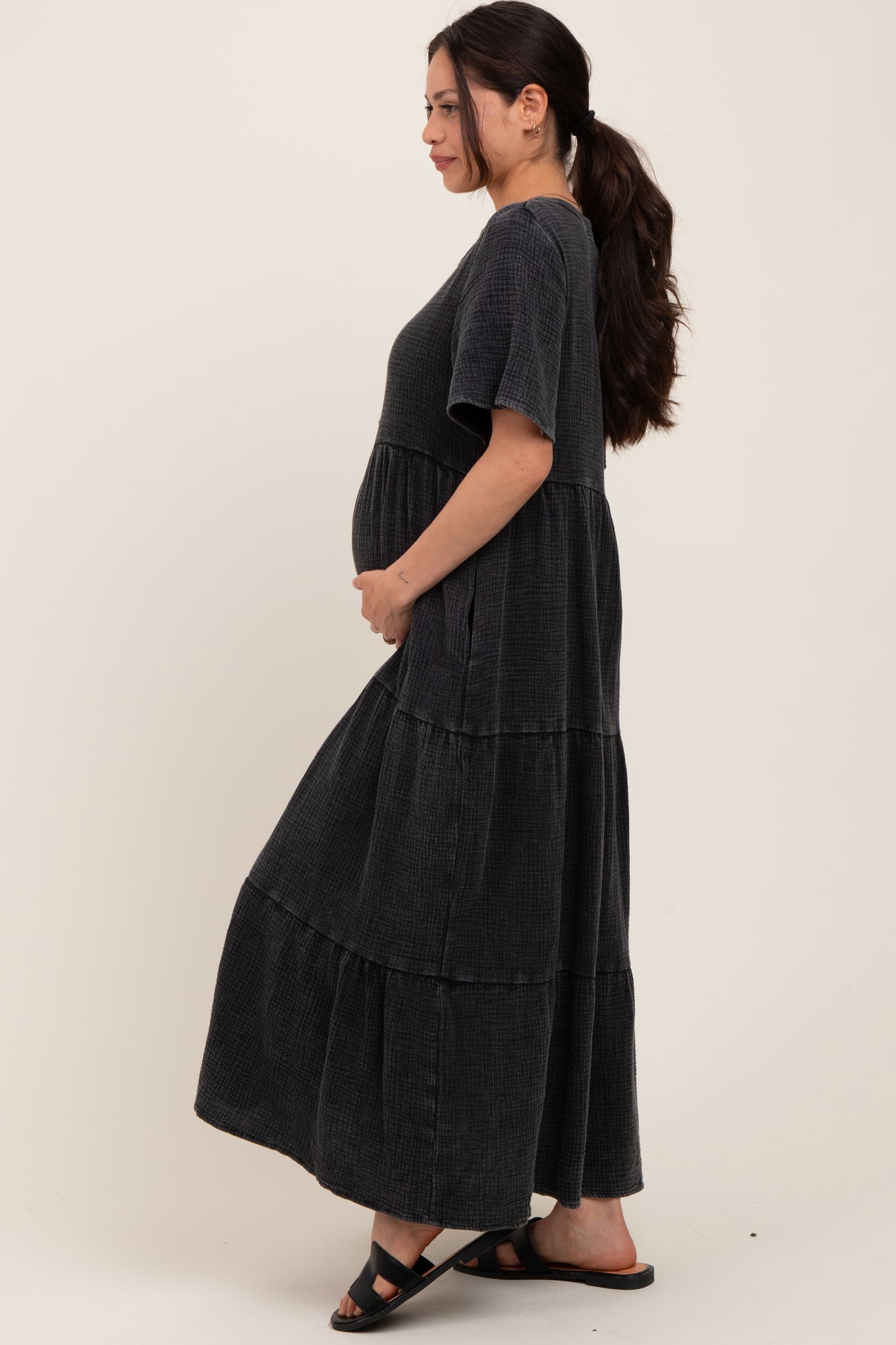 woman wearing a black tiered maternity dress, gently cradling her baby bump