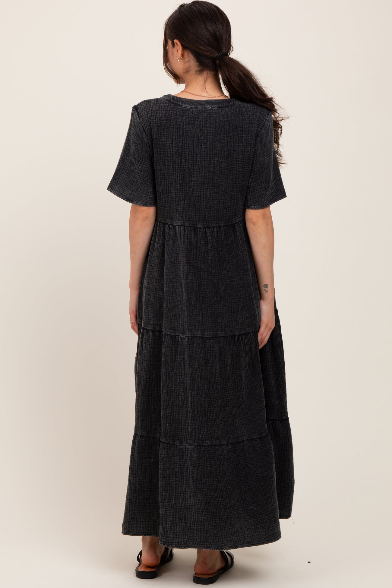 a woman wearing a black maxi maternity dress with short sleeves and tiered design, showing her back view
