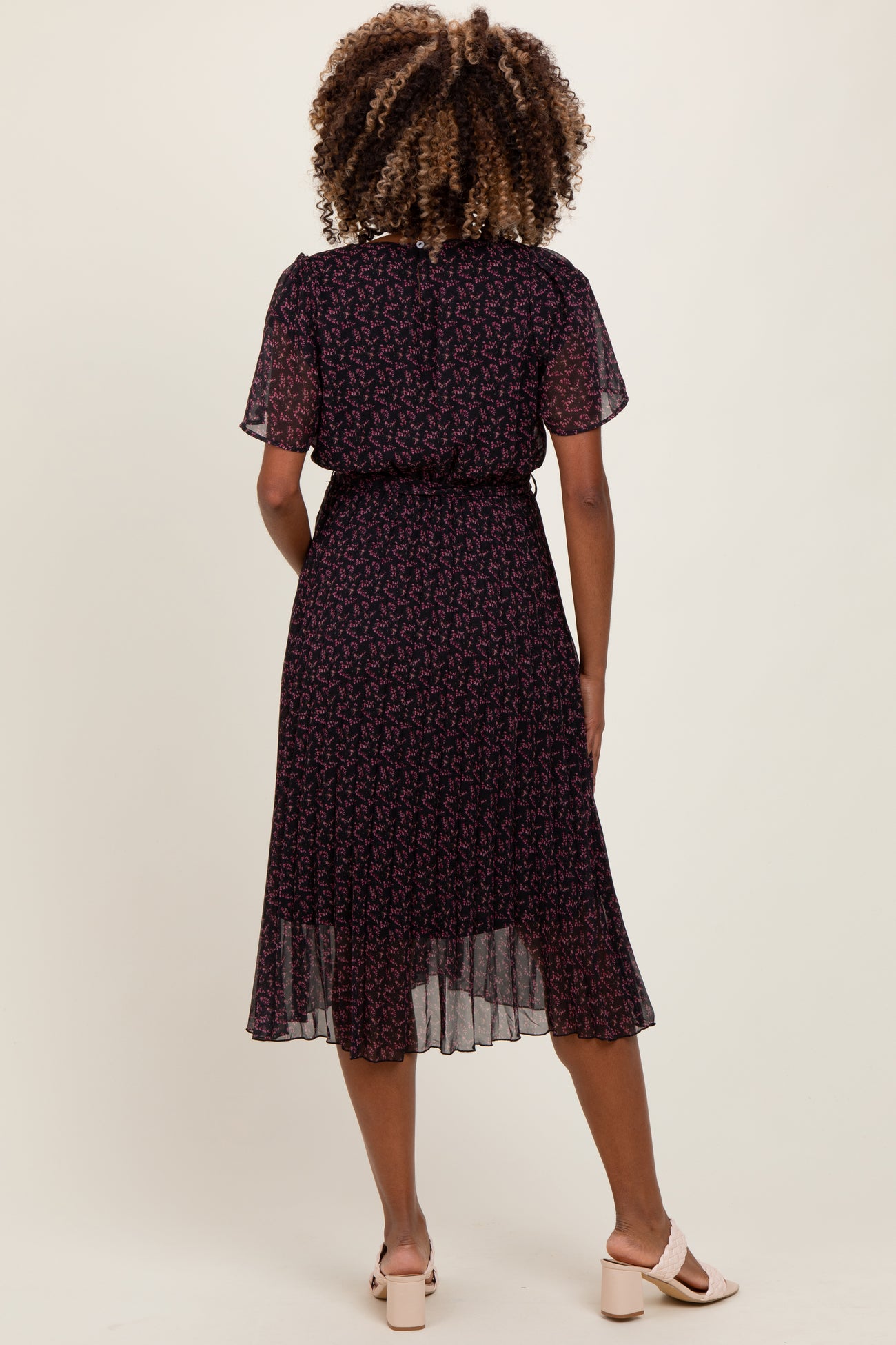 woman wearing a dark floral maternity dress with short sleeves and a flowy hem, showing a baby bump from the back