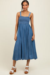 woman wearing a denim blue smocked maxi dress with thick straps and a flowy skirt, paired with white chunky heels