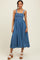 woman wearing a denim blue smocked maxi dress with thick straps and a flowy skirt, paired with white chunky heels