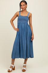 woman wearing a denim blue smocked maxi dress with wide straps and a flowy skirt