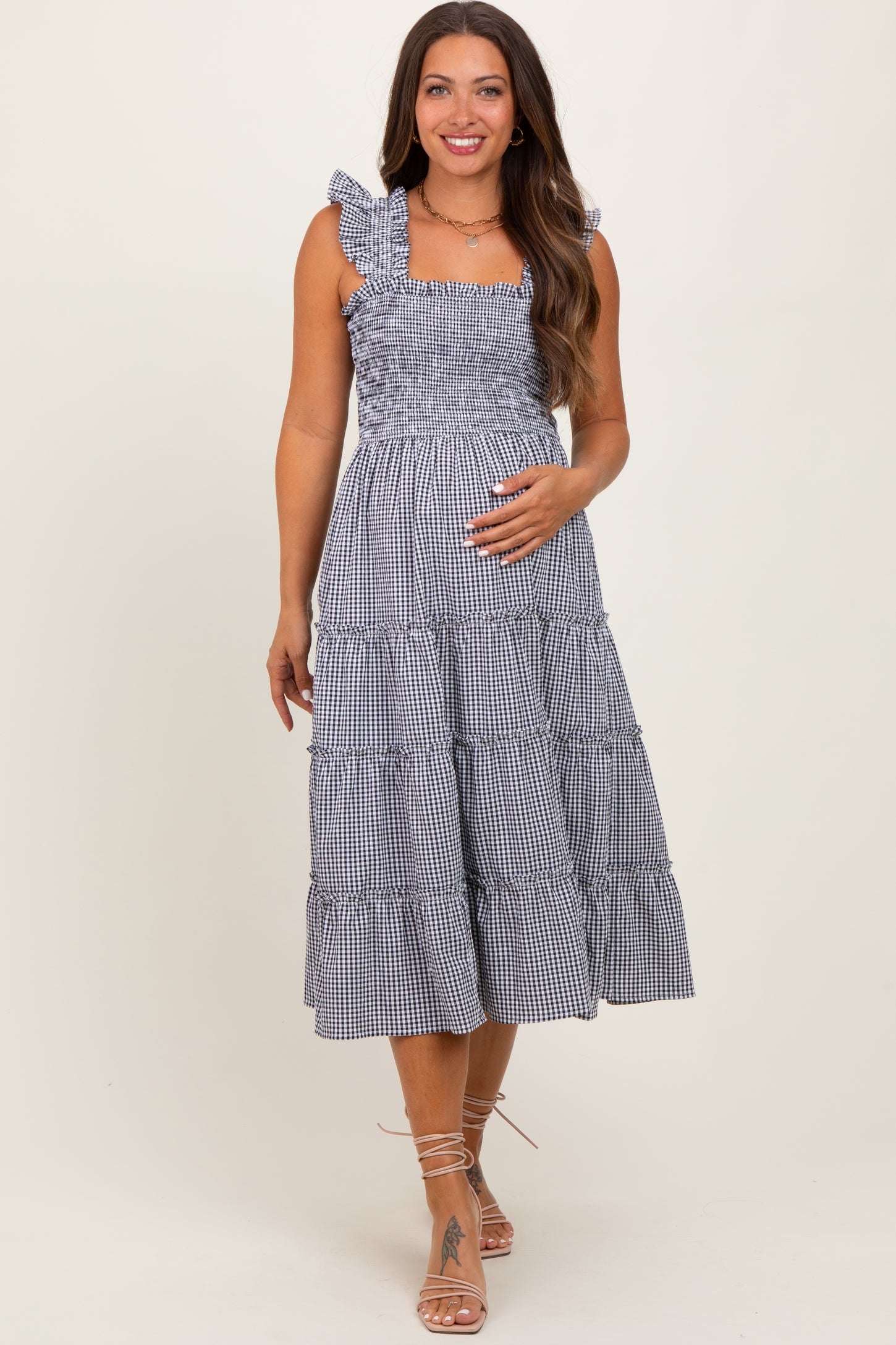 woman wearing a navy and white gingham maternity dress with ruffled straps and a tiered skirt, highlighting her baby bump