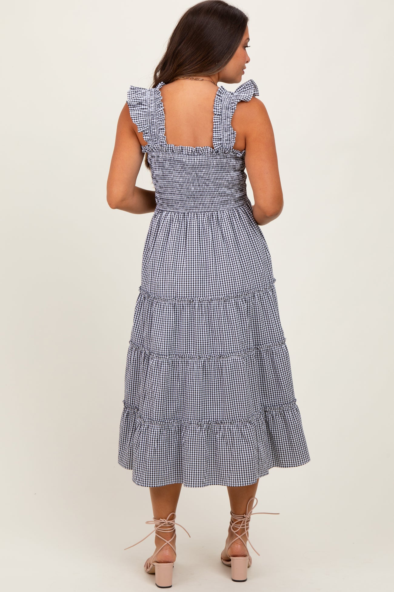 woman wearing a blue and white gingham maternity dress with ruffled straps and a tiered skirt, showing a baby bump from the back