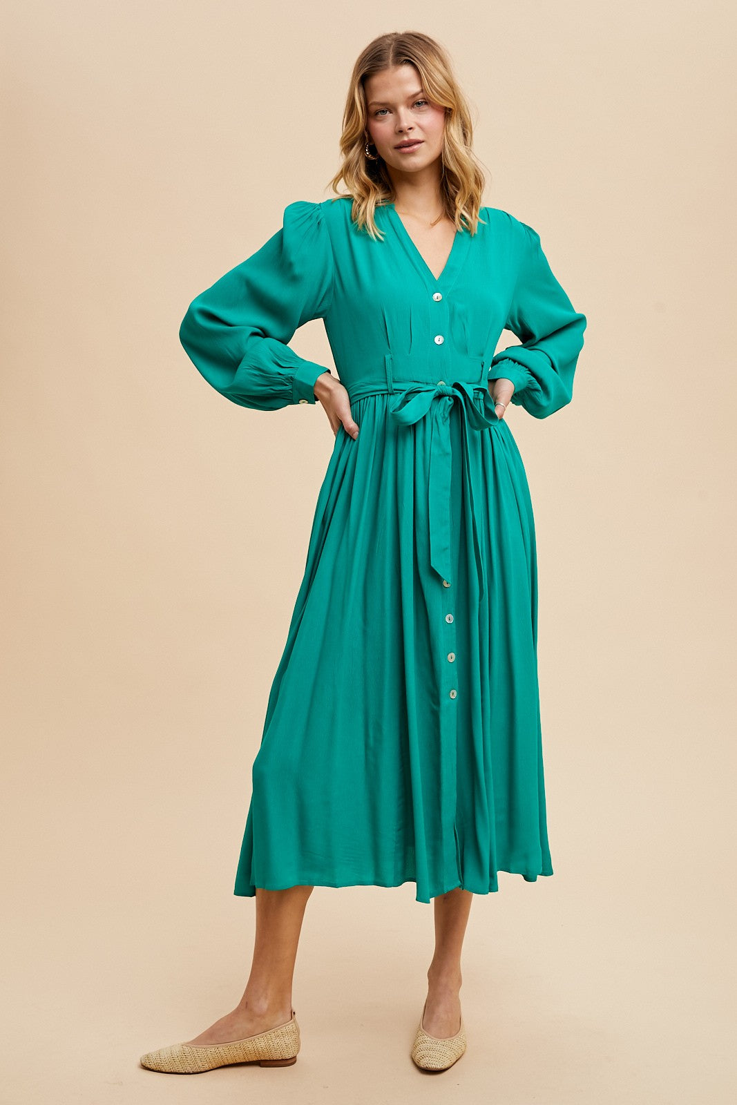 woman wearing a teal long sleeve button-up dress with a cinched waist and flowing skirt