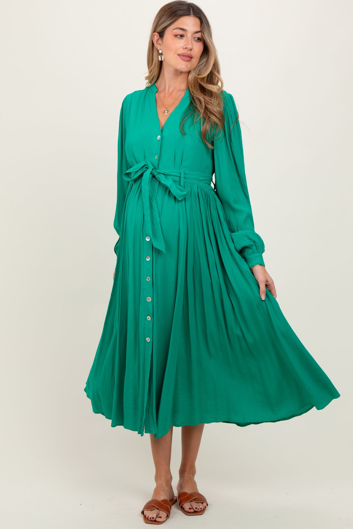 woman wearing a green maternity dress with a tie waist and button-down front, flowing skirt, and long sleeves