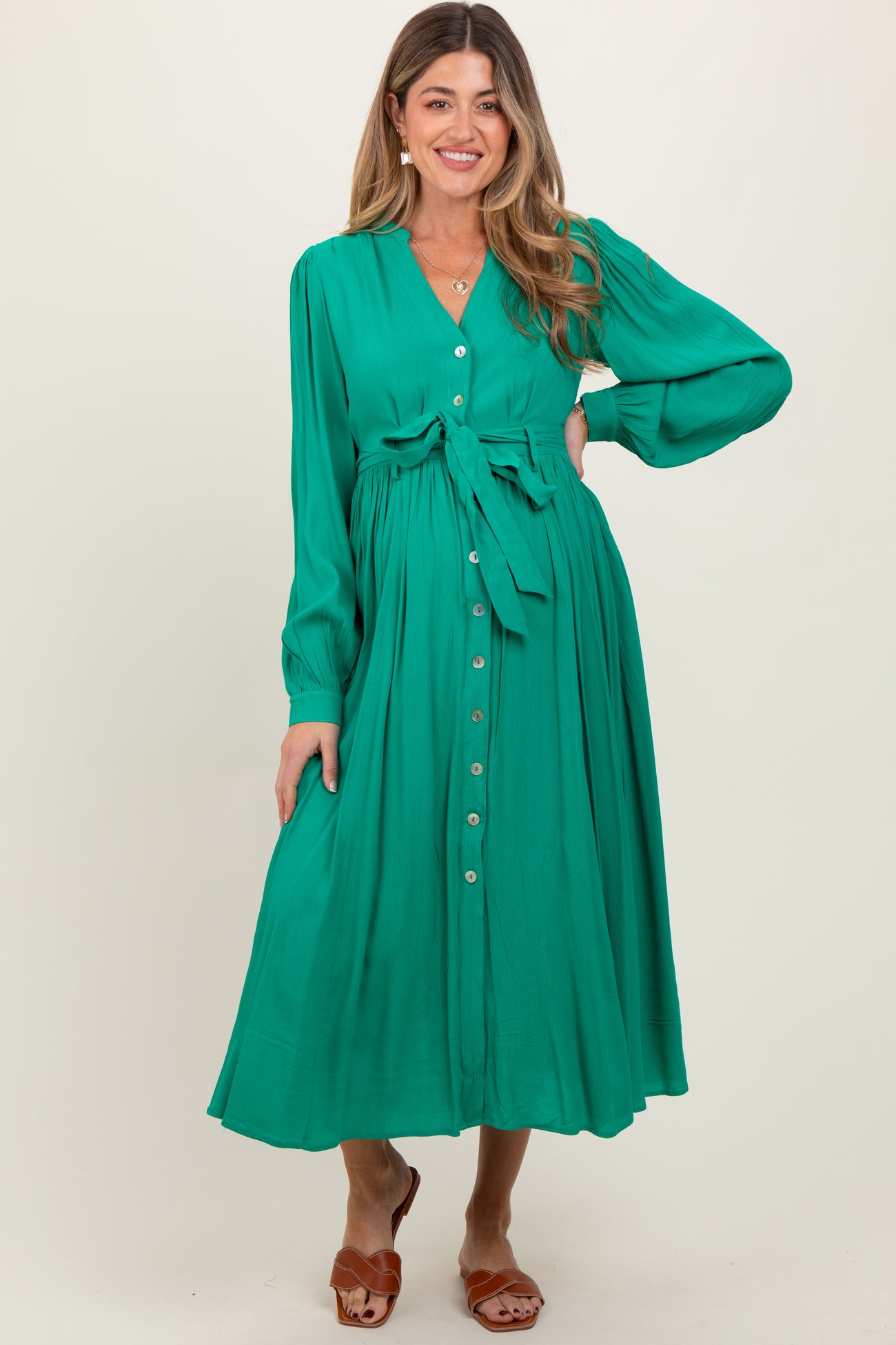 woman wearing a green button-up maternity dress with a tie waist and long sleeves, showing a baby bump