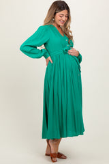 woman wearing a green long sleeve maternity dress with a knot detail, gently cradling her baby bump