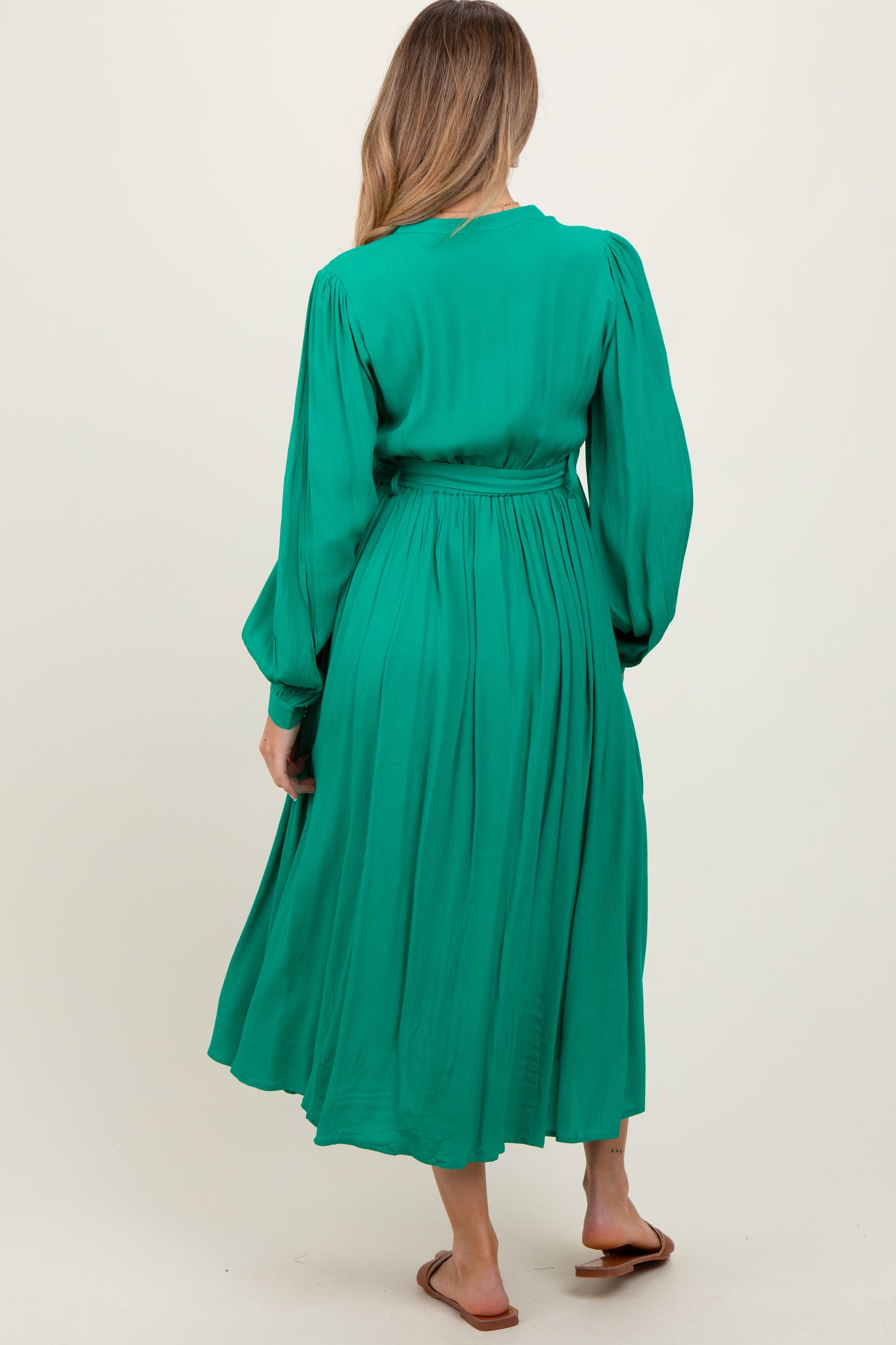 woman wearing a green long sleeve maternity dress with a cinched waist and flowy skirt, seen from the back