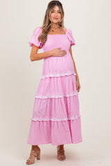woman wearing a pink striped maternity maxi dress with puff sleeves and tiered ruffle details, holding her baby bump