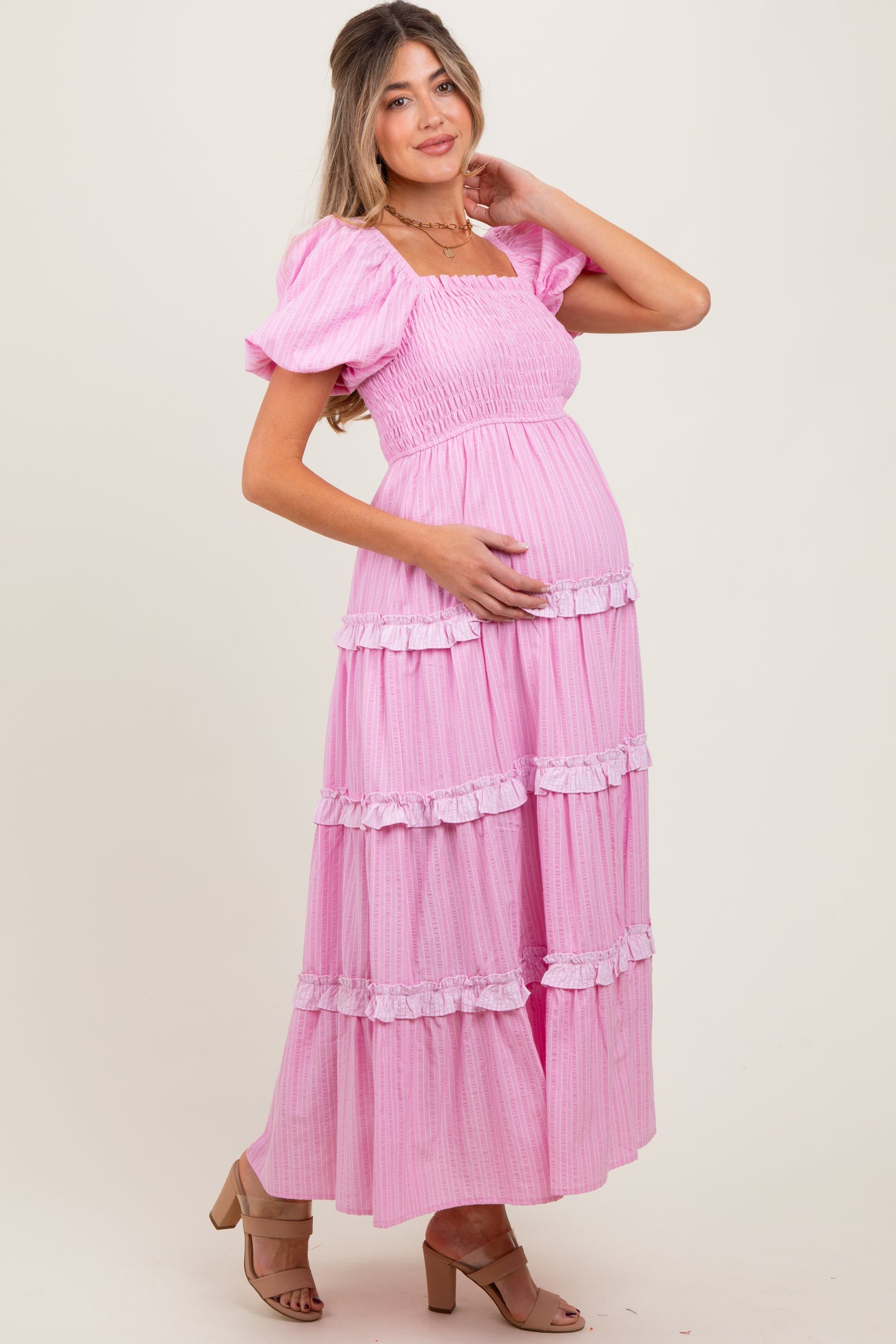 woman wearing a pink tiered maternity dress with puff sleeves and ruffle details, holding her baby bump