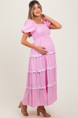 woman wearing a pink tiered maternity dress with puff sleeves and ruffle details, holding her baby bump