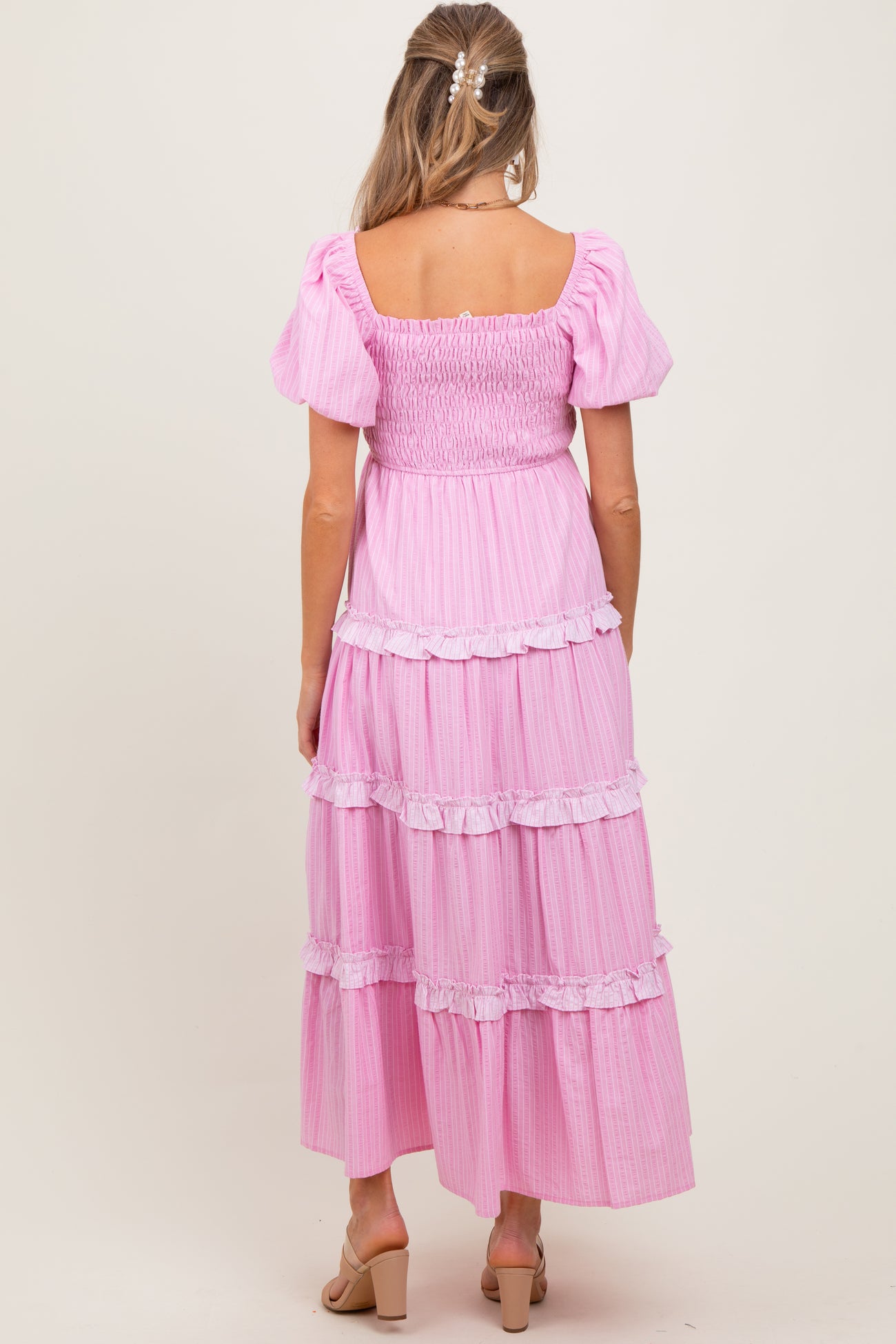 woman wearing a pink striped maternity maxi dress with puff sleeves and tiered ruffle details, viewed from the back