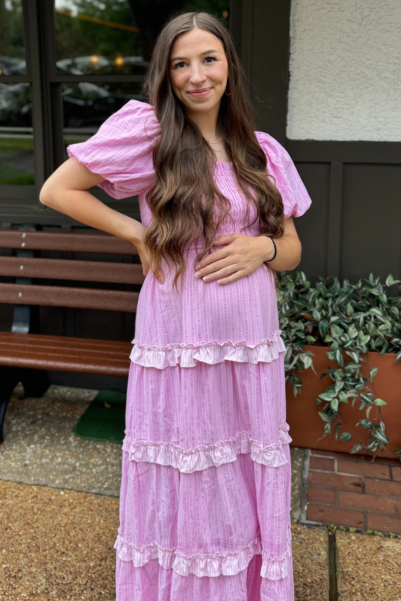 woman wearing a light pink tiered maternity dress with puff sleeves, holding her baby bump