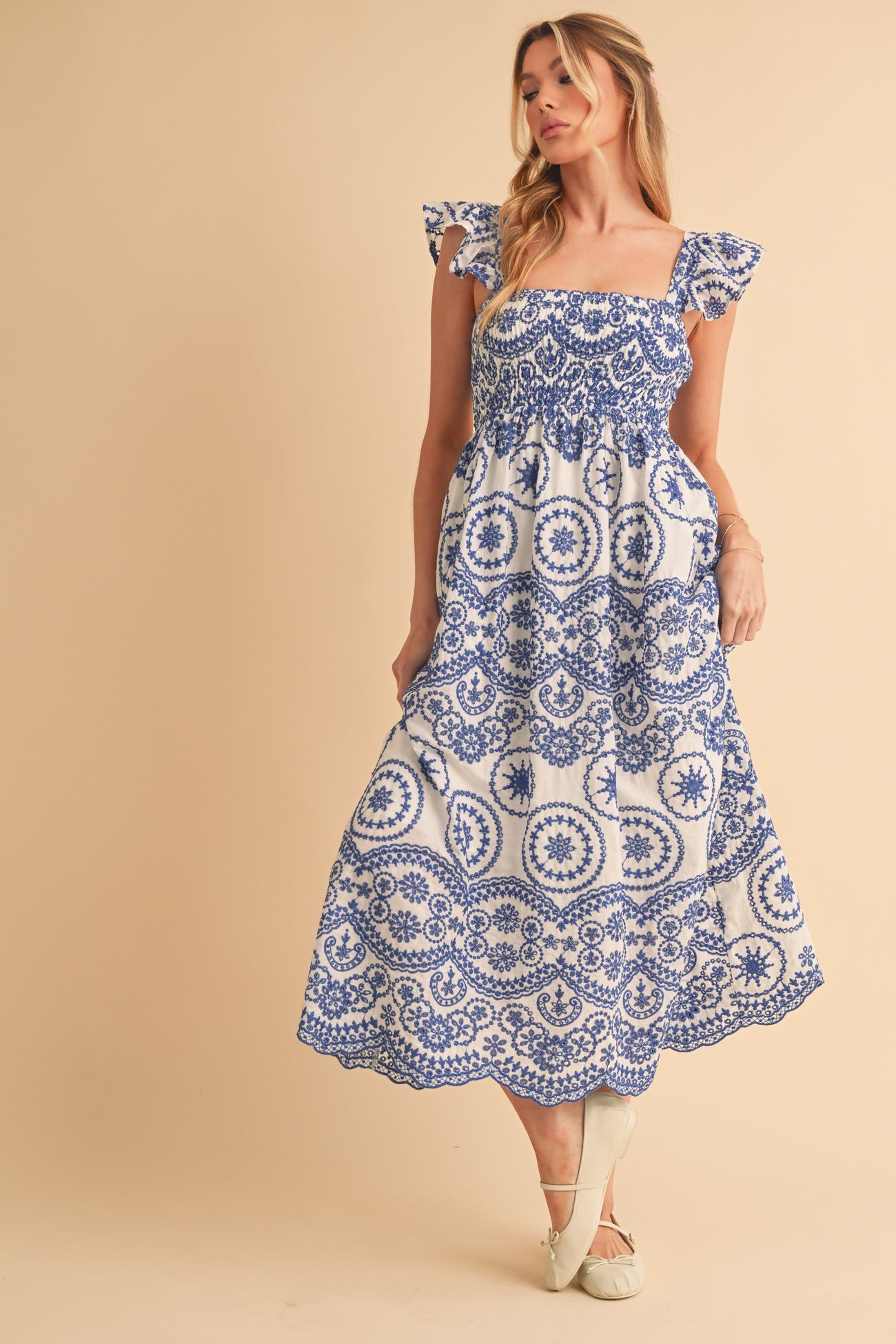 woman wearing a white off-the-shoulder maxi dress with blue floral patterns and ruffle sleeves