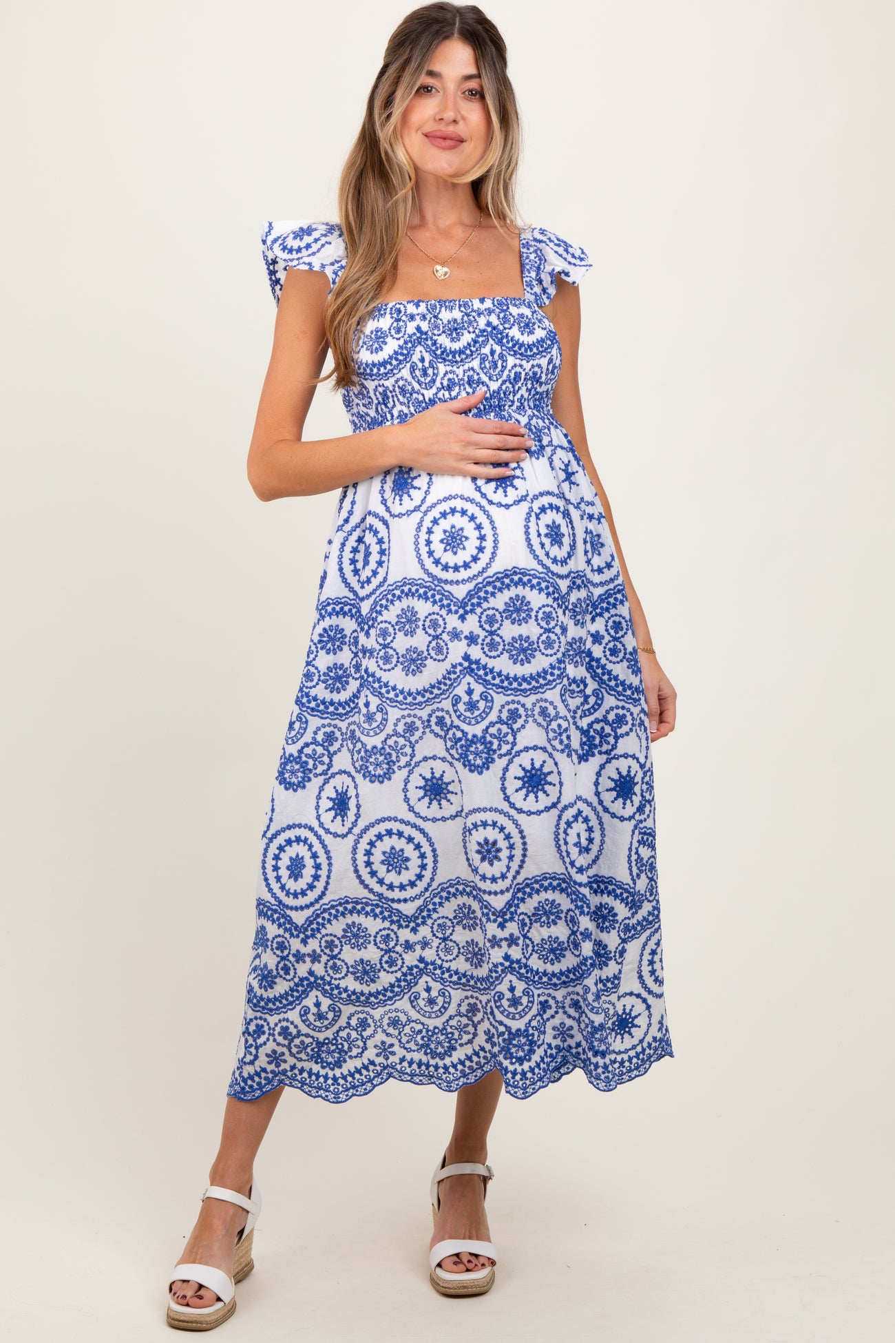 woman wearing a blue and white patterned maternity maxi dress with ruffled sleeves and holding her baby bump