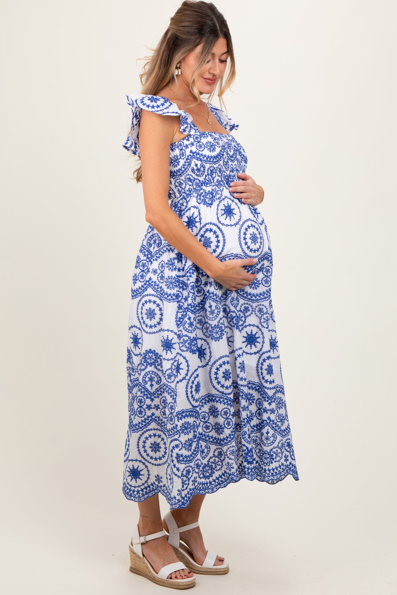 woman wearing a blue and white patterned maternity dress, holding her baby bump, with ruffled straps and a flowy hem