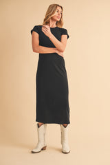 woman wearing a black cap sleeve midi dress and white cowboy boots, posing against a neutral background