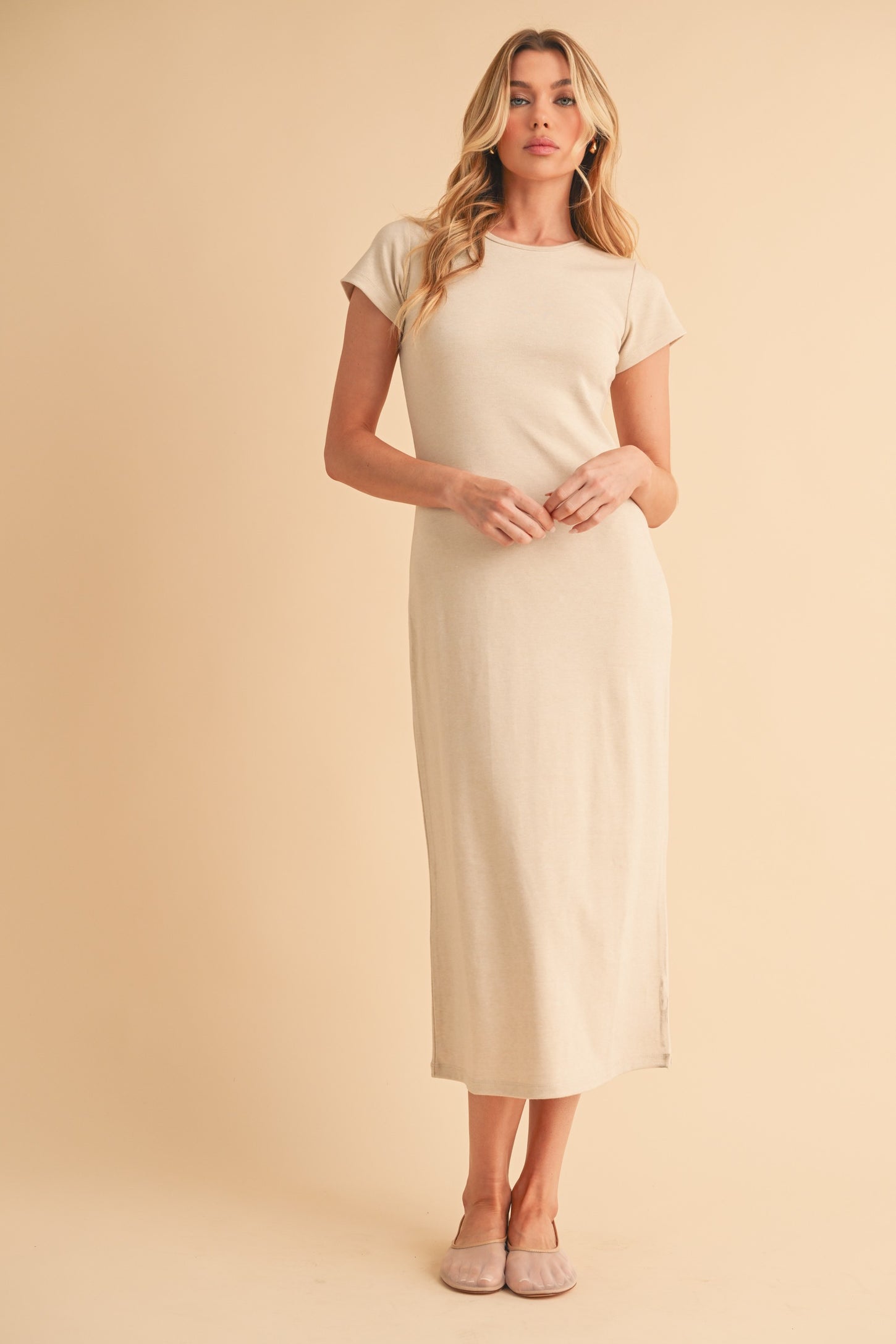 woman wearing a beige fitted midi dress with short sleeves and side slits, standing against a neutral background