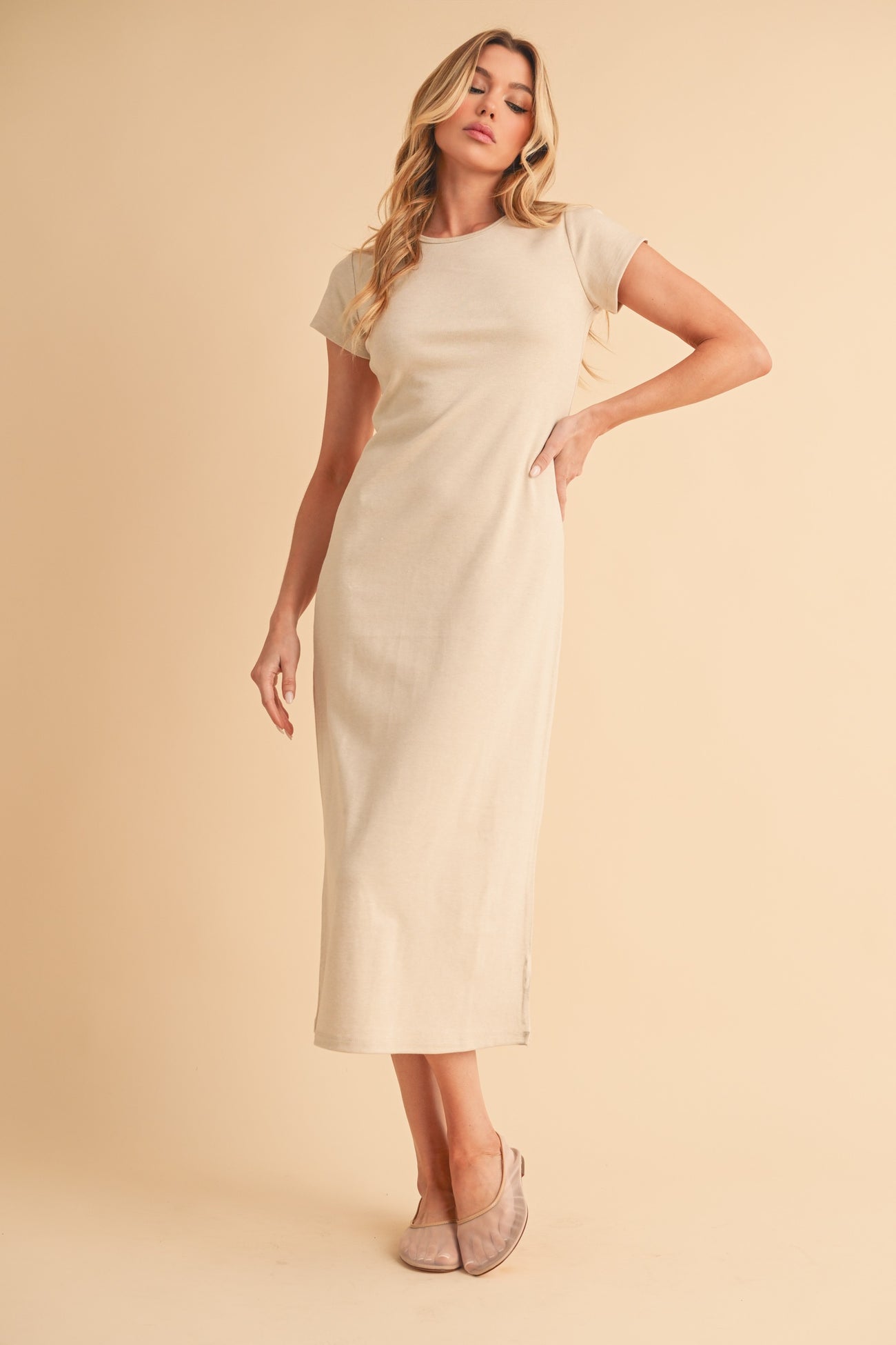 woman wearing a beige short sleeve maxi dress, standing elegantly with one hand on her hip