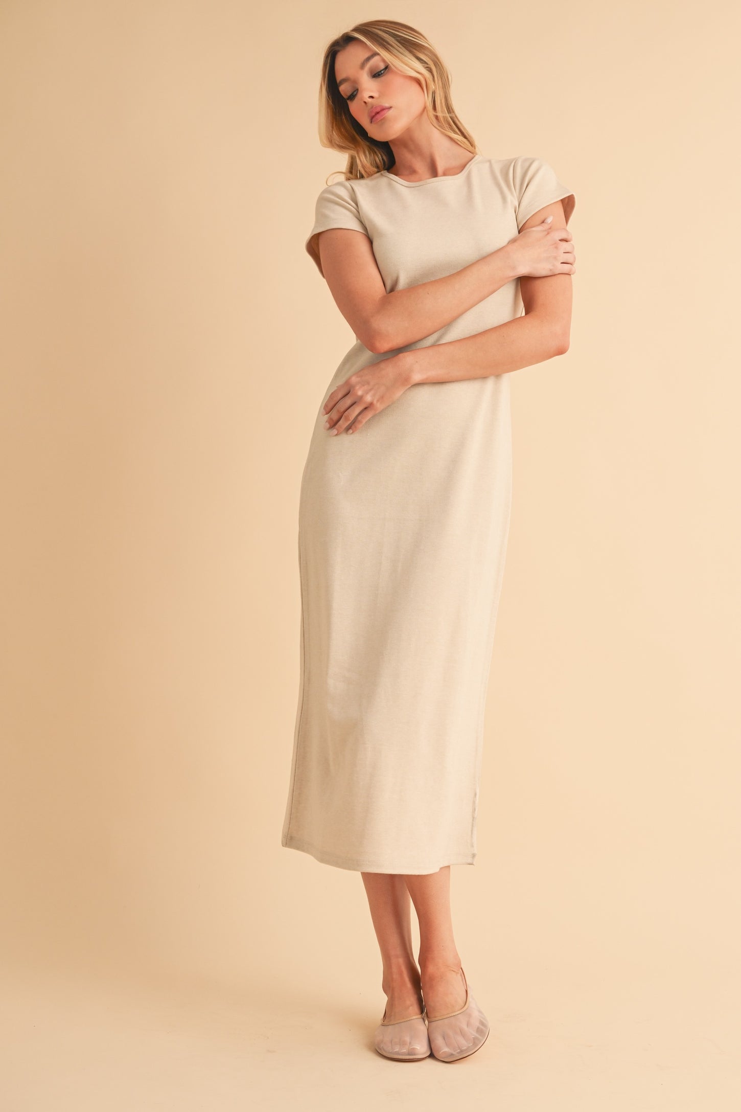 woman wearing a beige short sleeve maxi dress with a slightly fitted silhouette and side slits