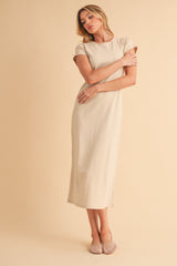 woman wearing a beige short sleeve maxi dress with a slightly fitted silhouette and side slits