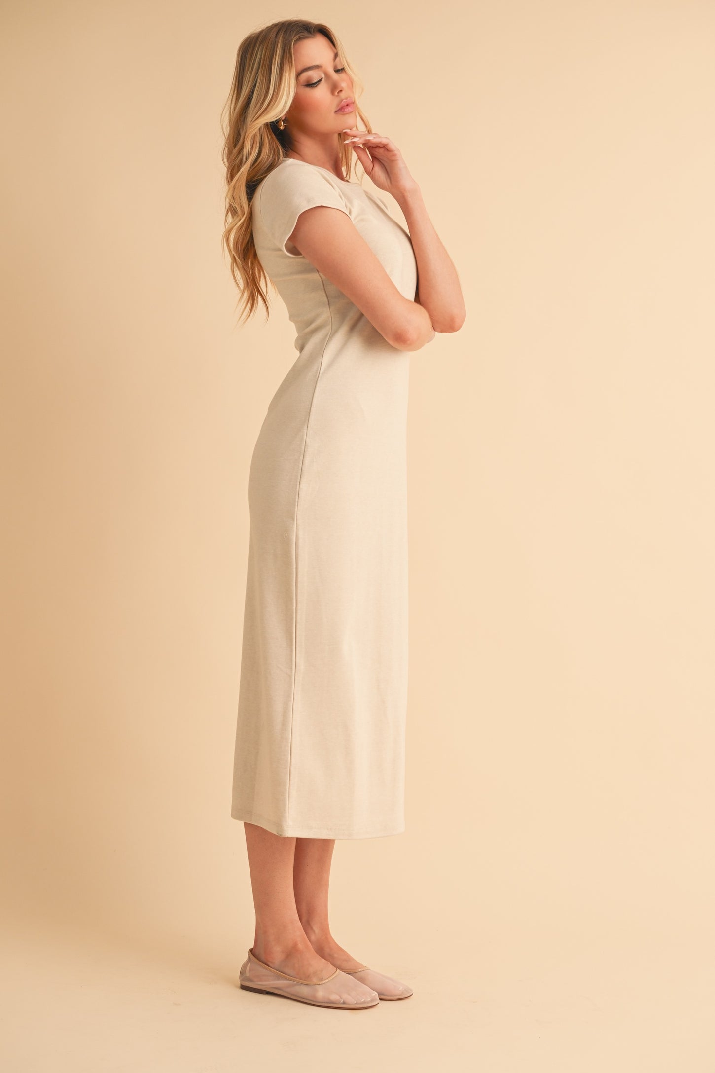 woman wearing a light beige short sleeve midi dress with a fitted silhouette and side slits