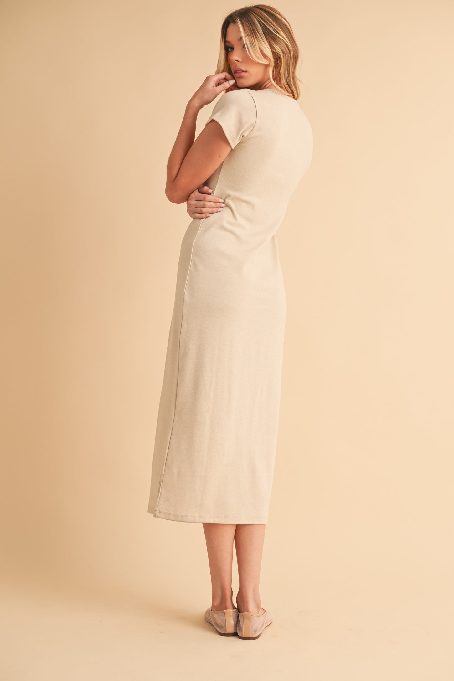 woman wearing a beige short sleeve maxi dress, standing with her back to the camera and arms crossed