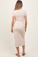woman wearing a light beige short sleeve maternity dress, showing a fitted style and mid-length hem, viewed from the back