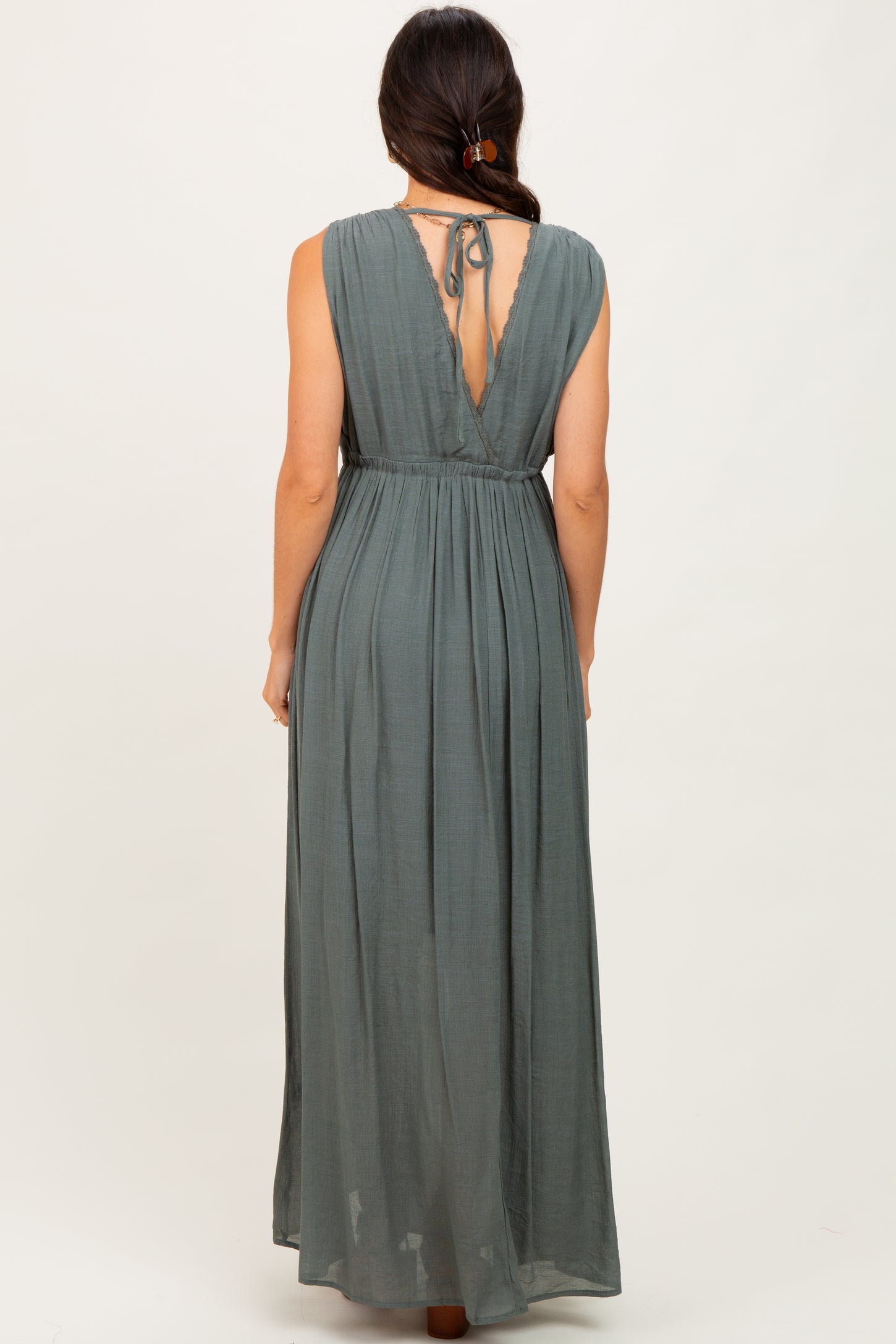 woman wearing a dusty green backless maxi dress with a tied detail at the neck and a flowy skirt