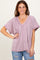 woman wearing a light mauve oversized v-neck top with short sleeves and front seam detailing, paired with ripped jeans