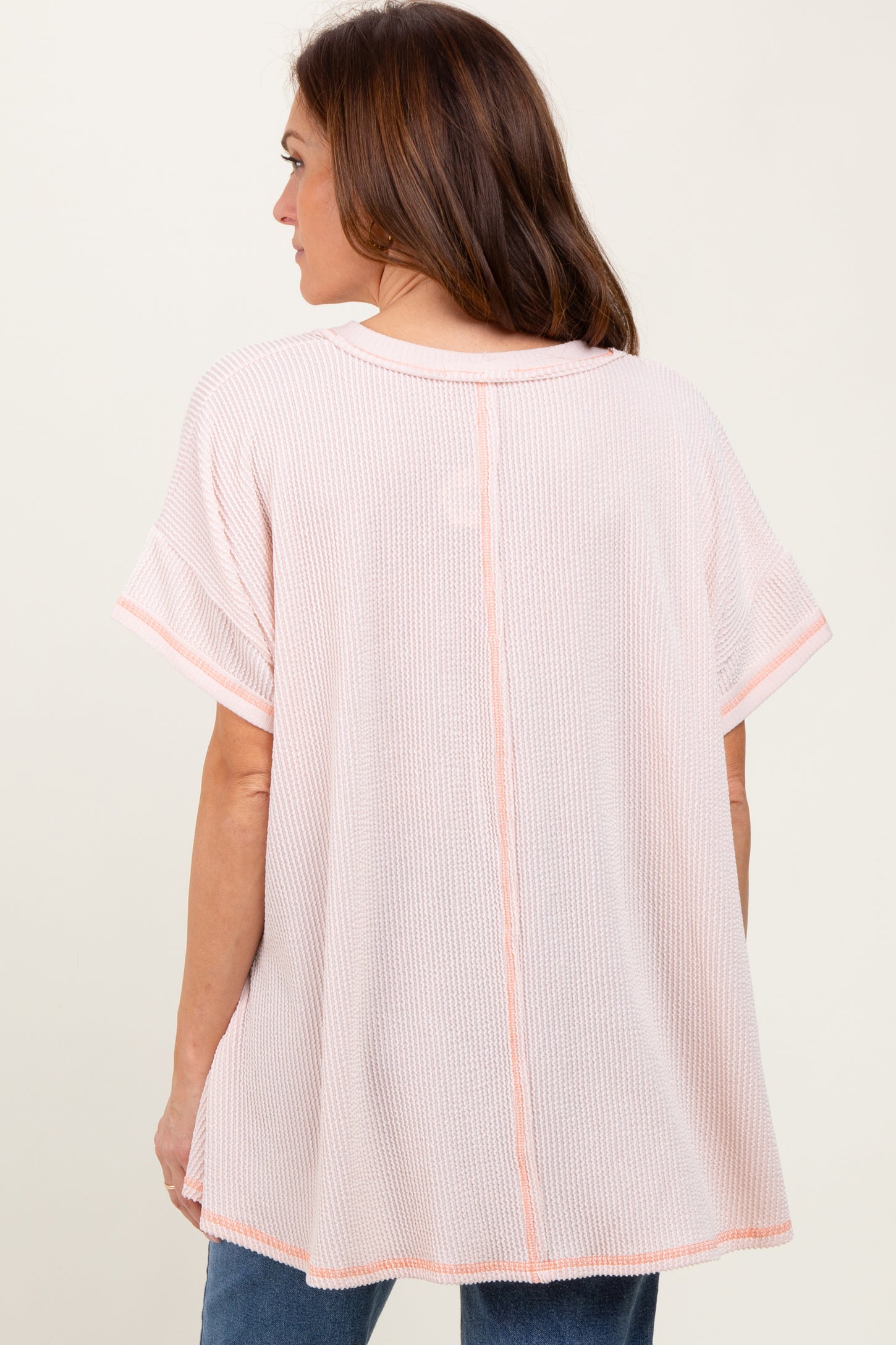 woman wearing a light pink oversized top with short sleeves and a back seam detail, styled with denim jeans