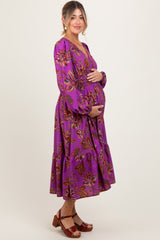 woman wearing a purple floral maternity dress with a baby bump, standing sideways and smiling