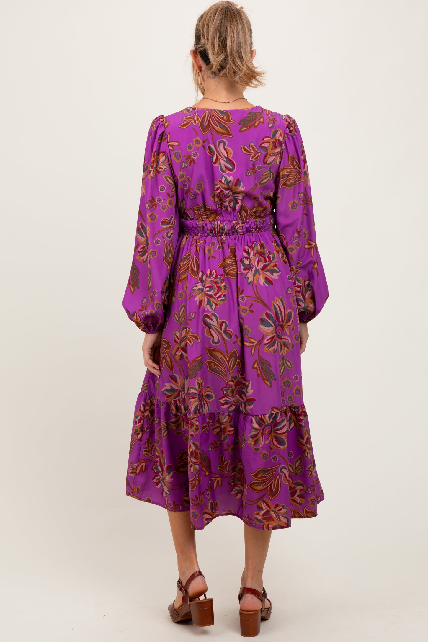 woman wearing a purple floral maternity dress with long sleeves and a tiered hem, showing a baby bump from the back