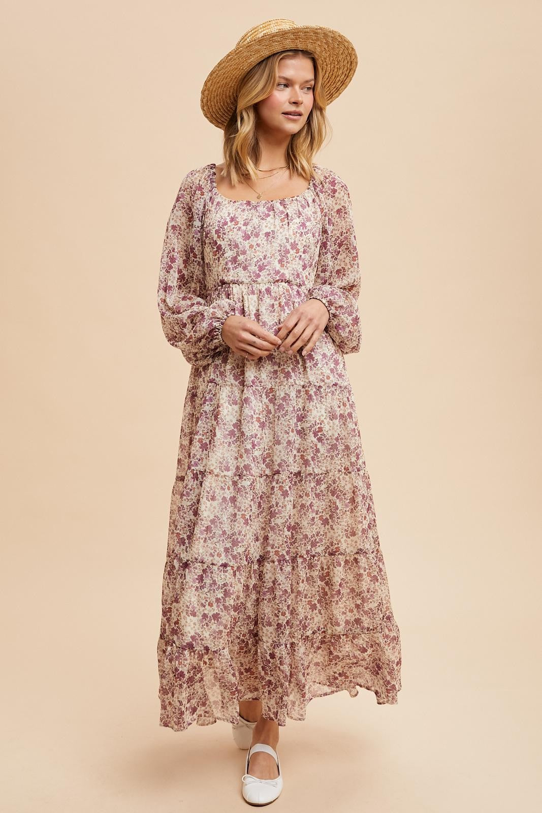 woman wearing a long floral maxi dress with long sleeves and a square neckline, paired with a straw hat