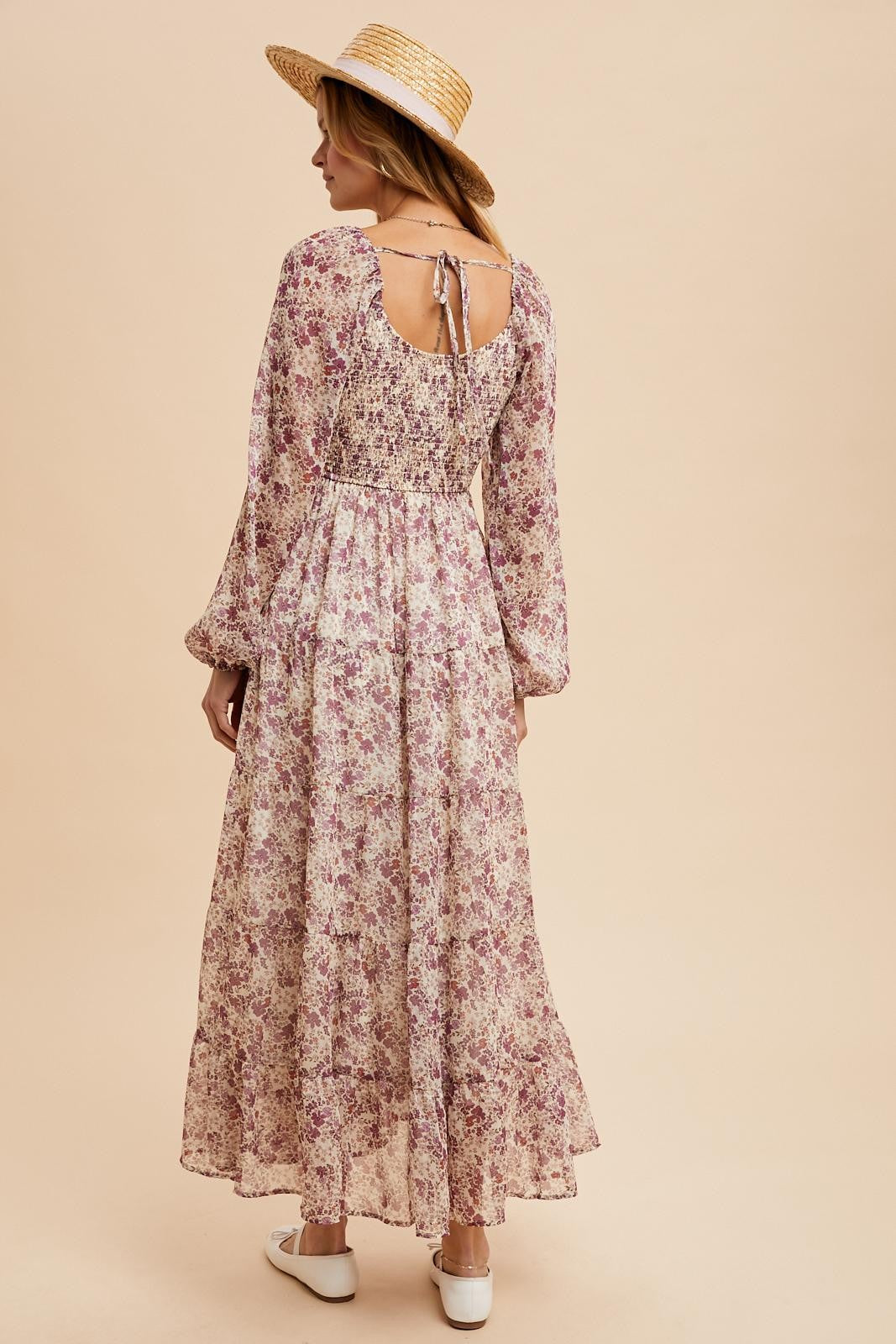 woman wearing a long floral maxi dress with long sleeves and a tie-back detail, styled with a straw hat