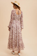 woman wearing a long floral maxi dress with long sleeves and a tie-back detail, styled with a straw hat
