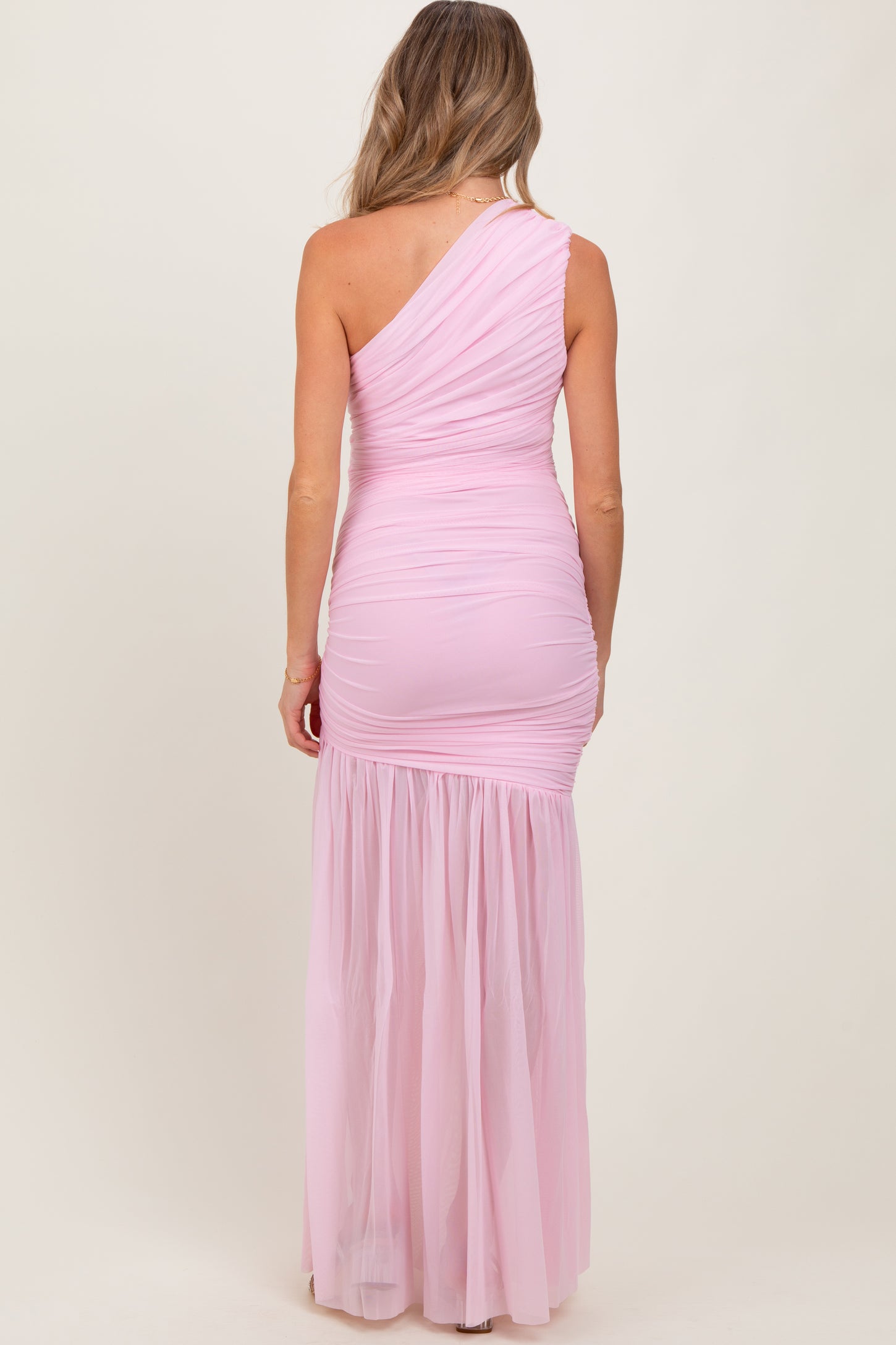 woman wearing a light pink one-shoulder maternity gown with a fitted bodice and flowing skirt