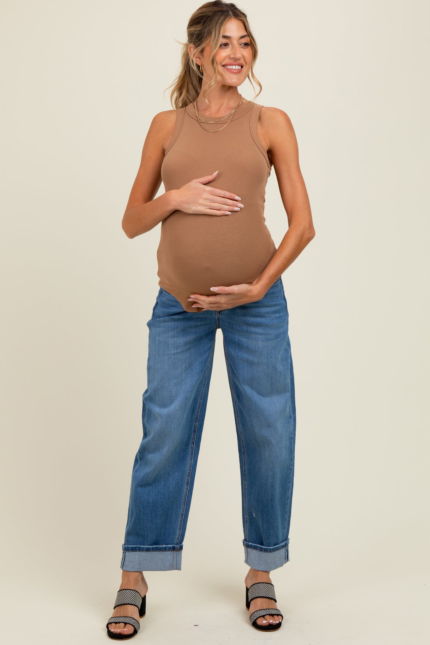 woman wearing a brown ribbed maternity tank top and blue relaxed fit jeans, holding her baby bump
